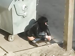 Drunk dark-haired girl urinates next to garbage